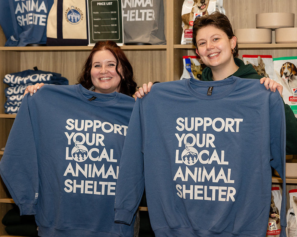 Two people holding blue sweatshirts with text in a store setting.